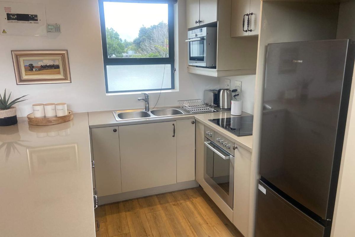 Compact modern kitchen featuring light-toned cabinetry, stone-look countertops, integrated oven, electric hob, and a double-basin sink with a window view.