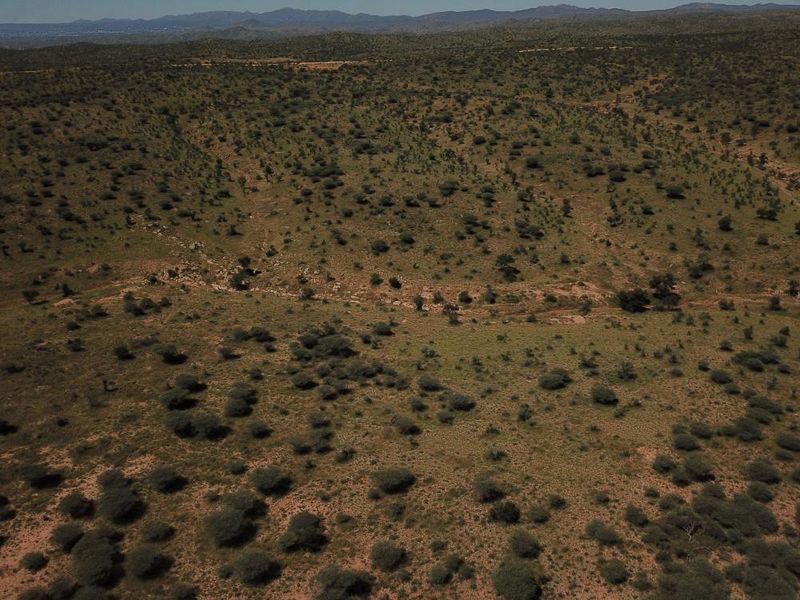 An aerial view of expansive, undeveloped residential land featuring natural vegetation and rolling terrain under a clear sky.