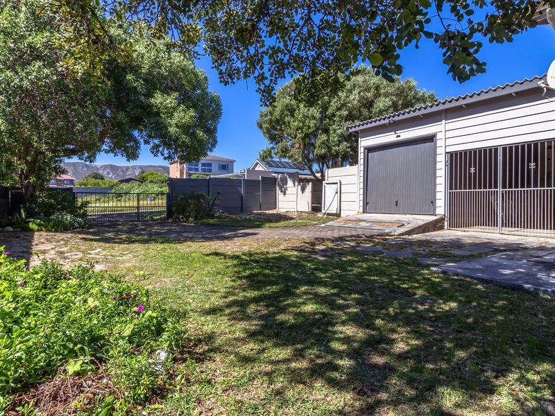 Rear exterior view featuring a garage, paved driveway, security gate, and boundary wall, set within a private garden area.