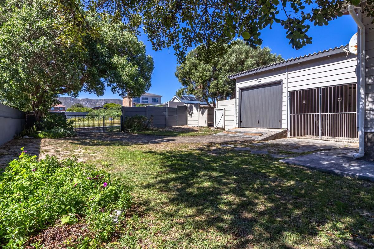 Rear exterior view featuring a garage, paved driveway, security gate, and boundary wall, set within a private garden area.