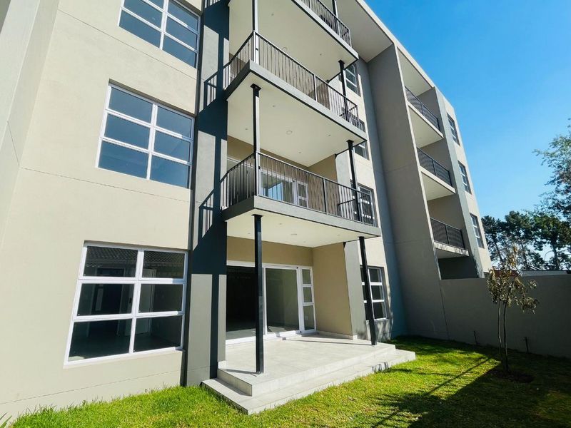Rear view of a modern apartment building featuring stacked balconies with metal railings, sliding glass doors, and a ground-level concrete patio area.