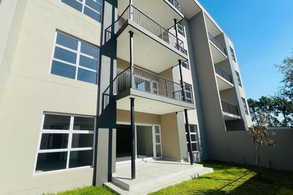 Rear view of a modern apartment building featuring stacked balconies with metal railings, sliding glass doors, and a ground-level concrete patio area.