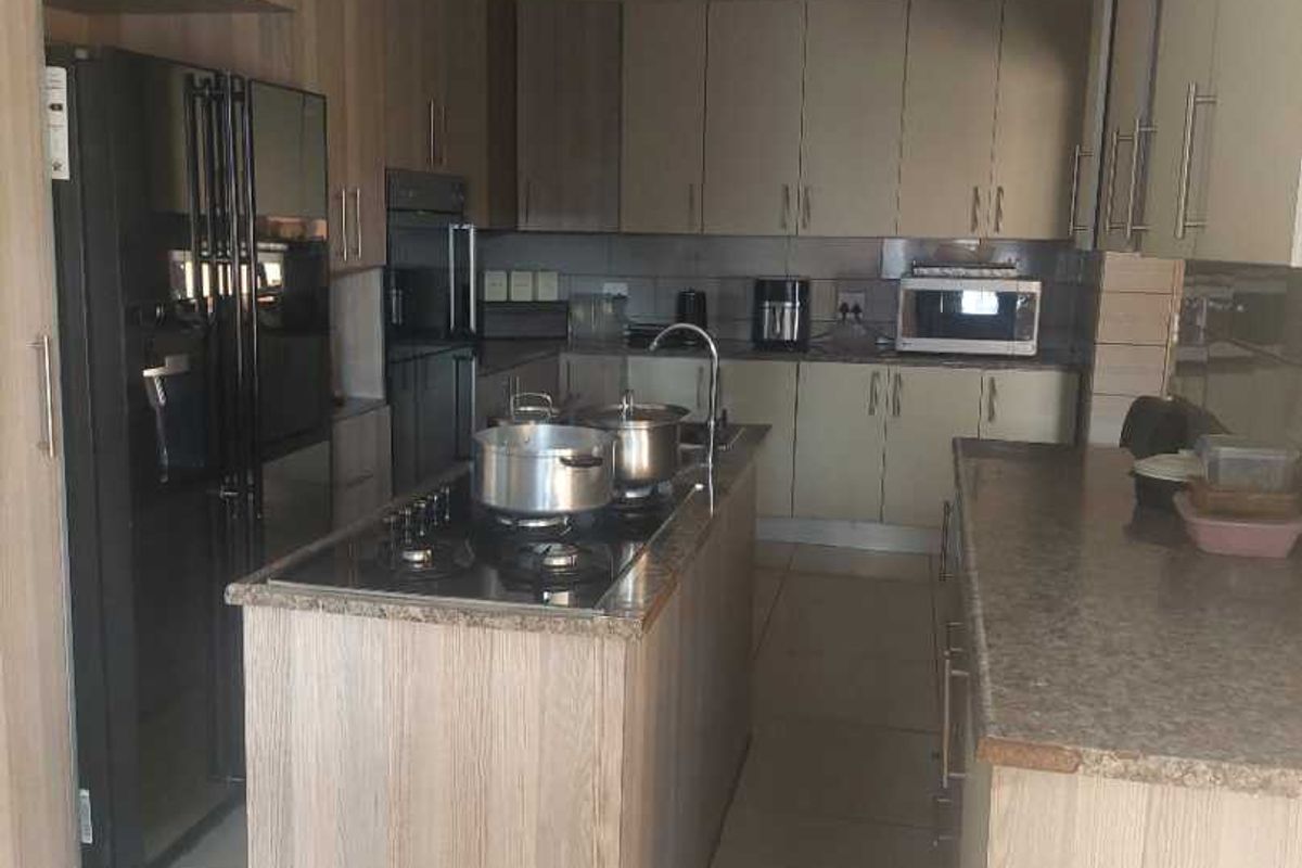 Modern kitchen featuring light wood-grain cabinetry, a central island with a gas hob, stone countertops, and tiled flooring.