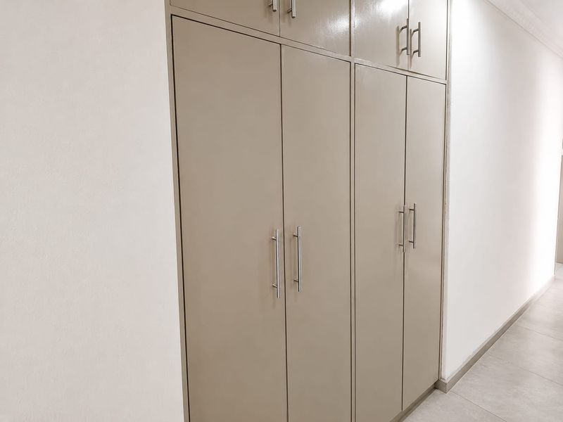 A clean hallway featuring neutral-toned built-in cupboards with modern hardware and light-colored floor tiles.