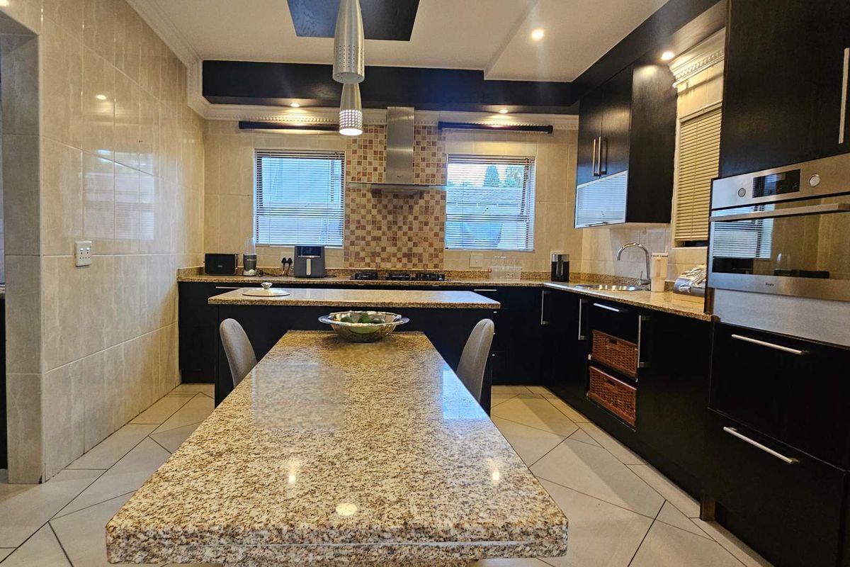 Modern kitchen featuring dark cabinetry, granite countertops, integrated oven, and a central island with breakfast bar seating.