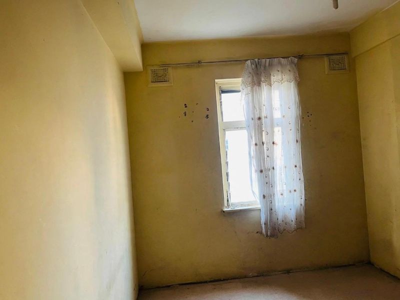 An empty bedroom featuring yellow walls with visible surface damage and ventilation grilles, requiring cosmetic updates and repairs.