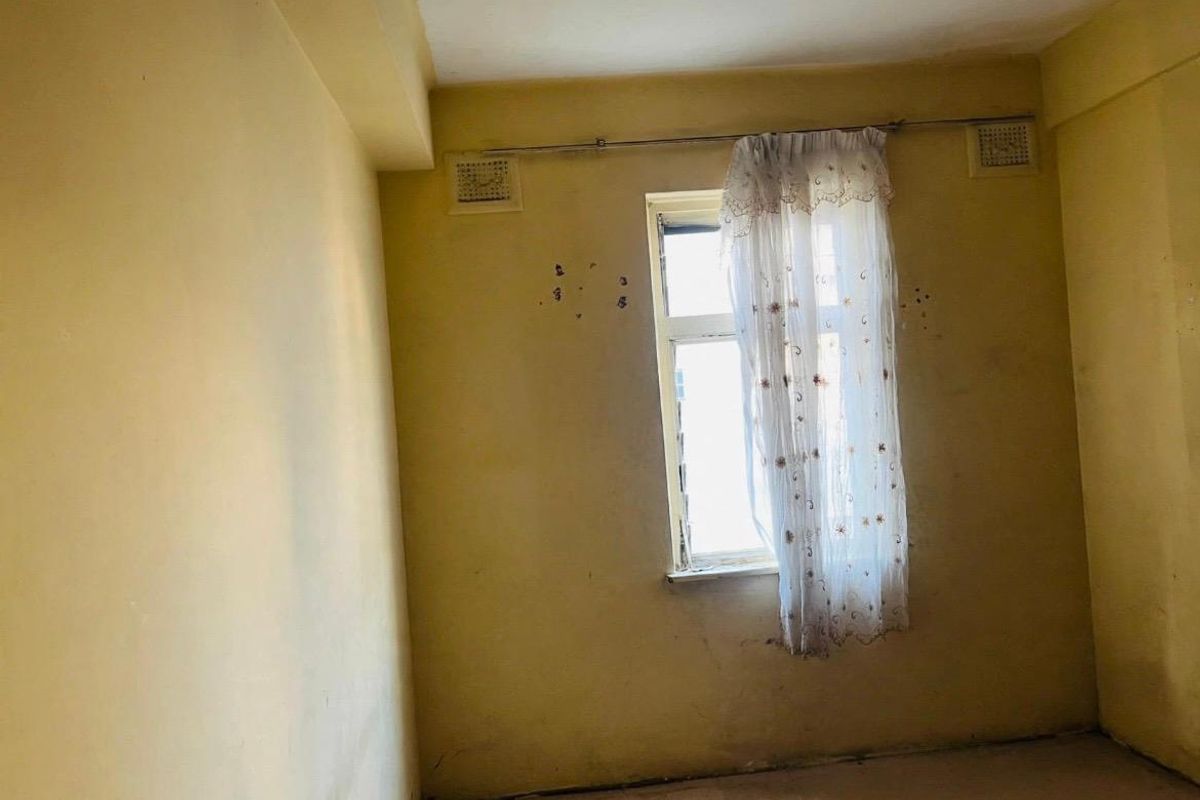 An empty bedroom featuring yellow walls with visible surface damage and ventilation grilles, requiring cosmetic updates and repairs.