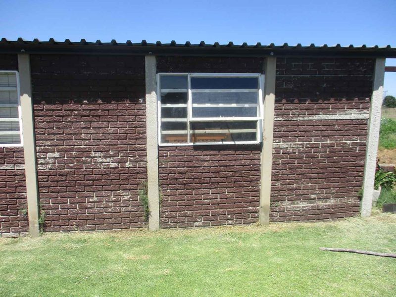Exterior view of a brick structure featuring concrete columns and aluminium framed windows, set against a grassed area.
