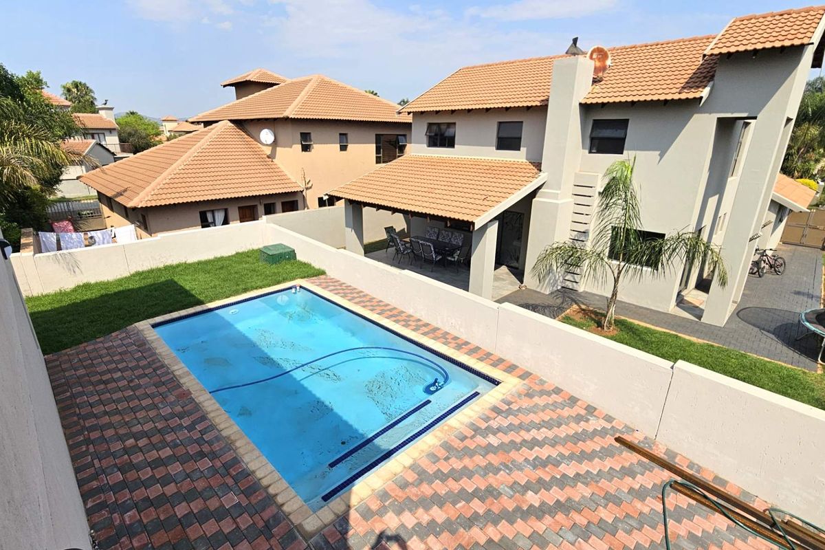 Elevated view of a residential backyard featuring a swimming pool, paved surround, lawn area, and a covered patio attached to the main house.