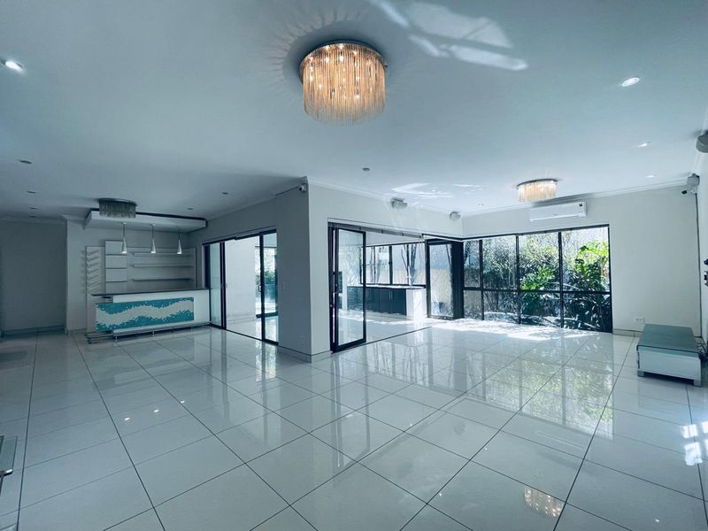 Spacious open-plan living area featuring polished porcelain tiles, a built-in bar, elegant chandeliers, and large glass doors opening to the garden.