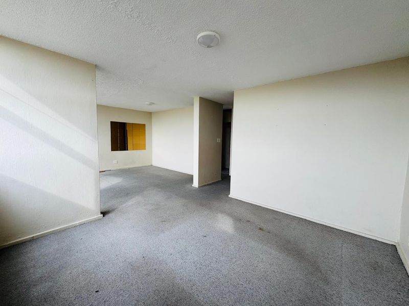 An empty, open-plan living area featuring neutral walls, carpeted flooring, and a unique internal wall cutout, offering a blank canvas for renovation.