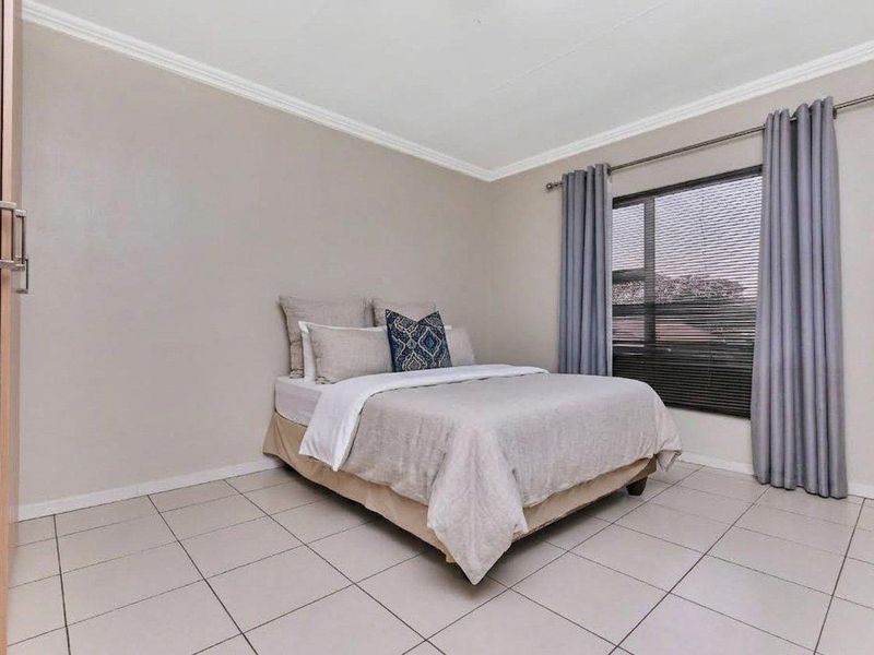 A well-maintained bedroom featuring neutral wall tones, tiled flooring, a built-in wardrobe, and window treatments including blinds and curtains.