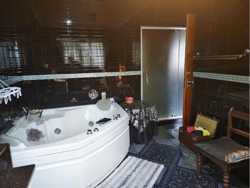 A bathroom featuring a corner spa bath, shower enclosure, and dark tiled finishes throughout.