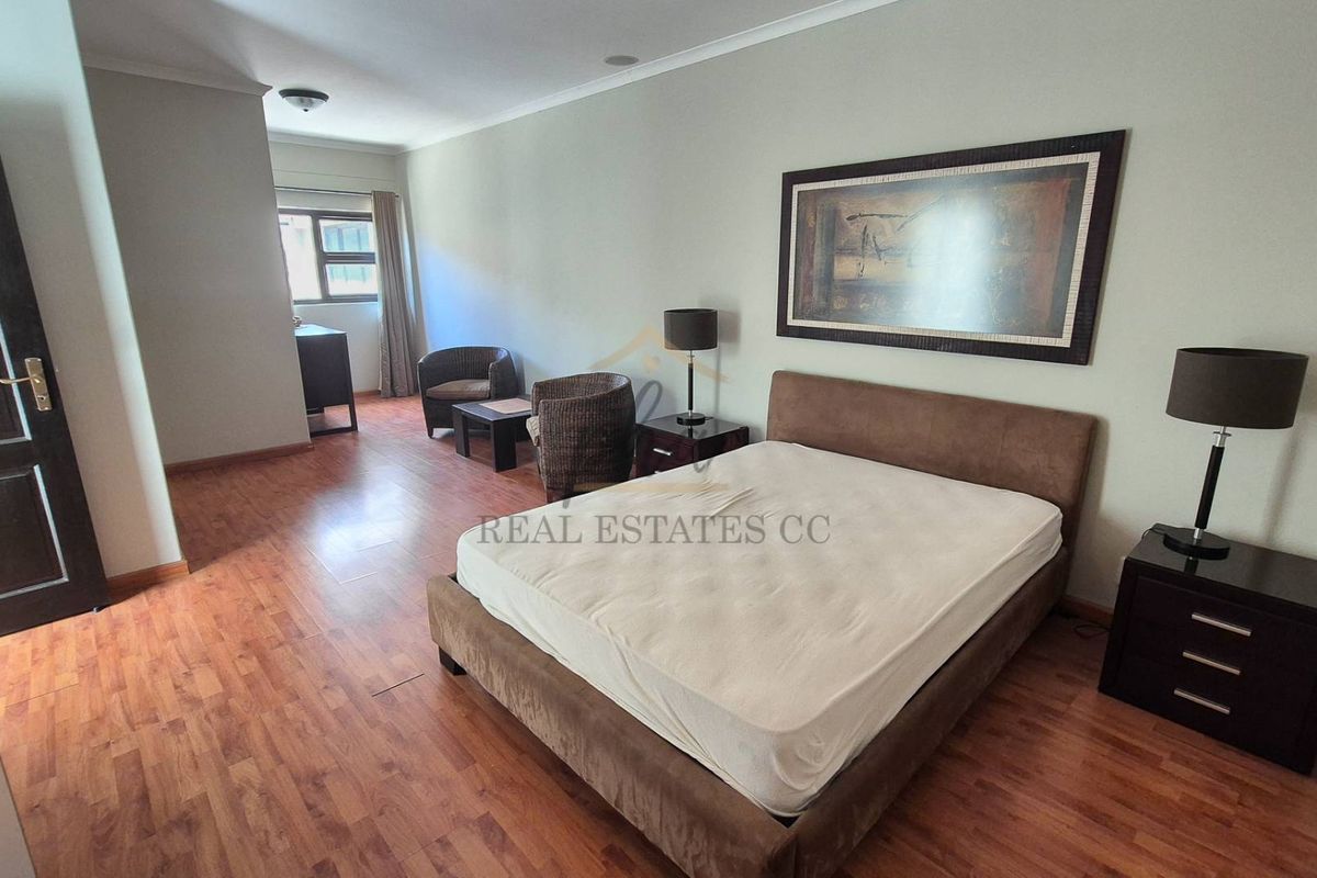 Spacious bedroom featuring wood-look laminate flooring, neutral wall finishes, and a functional layout with an integrated seating area.