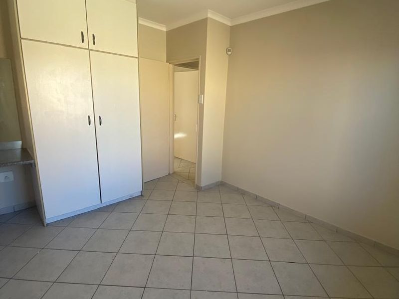 An empty bedroom featuring neutral tiled flooring, built-in cupboards with overhead storage, and a simple ceiling light fixture.