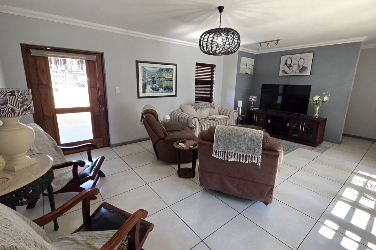 Spacious living room featuring light-colored floor tiles, neutral wall tones, and a timber-framed entrance door, offering a comfortable and well-lit living space.