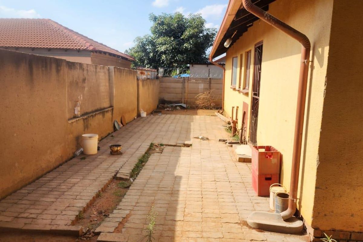 A side exterior area featuring paved ground, perimeter boundary walls, and a side entrance to the main dwelling structure.