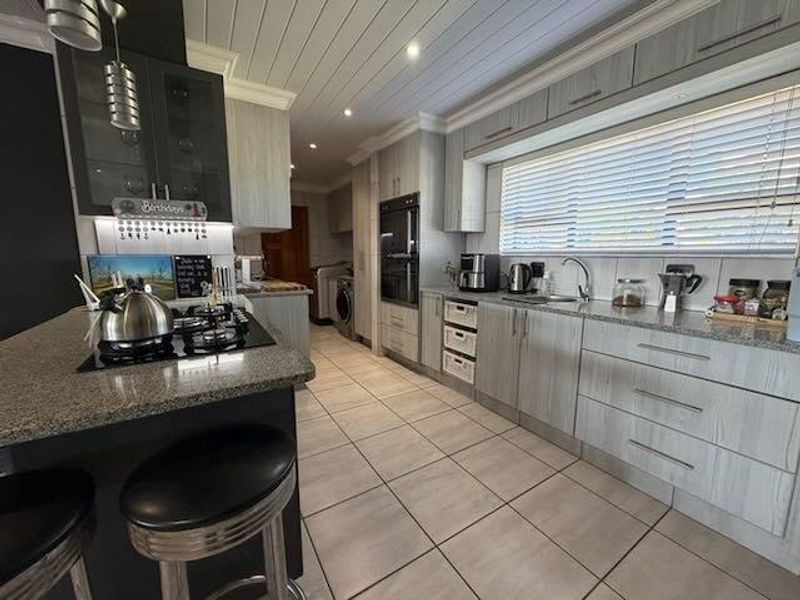 Modern kitchen featuring granite countertops, built-in oven, gas hob, and ample cabinetry, complemented by tiled flooring and a tongue and groove ceiling.
