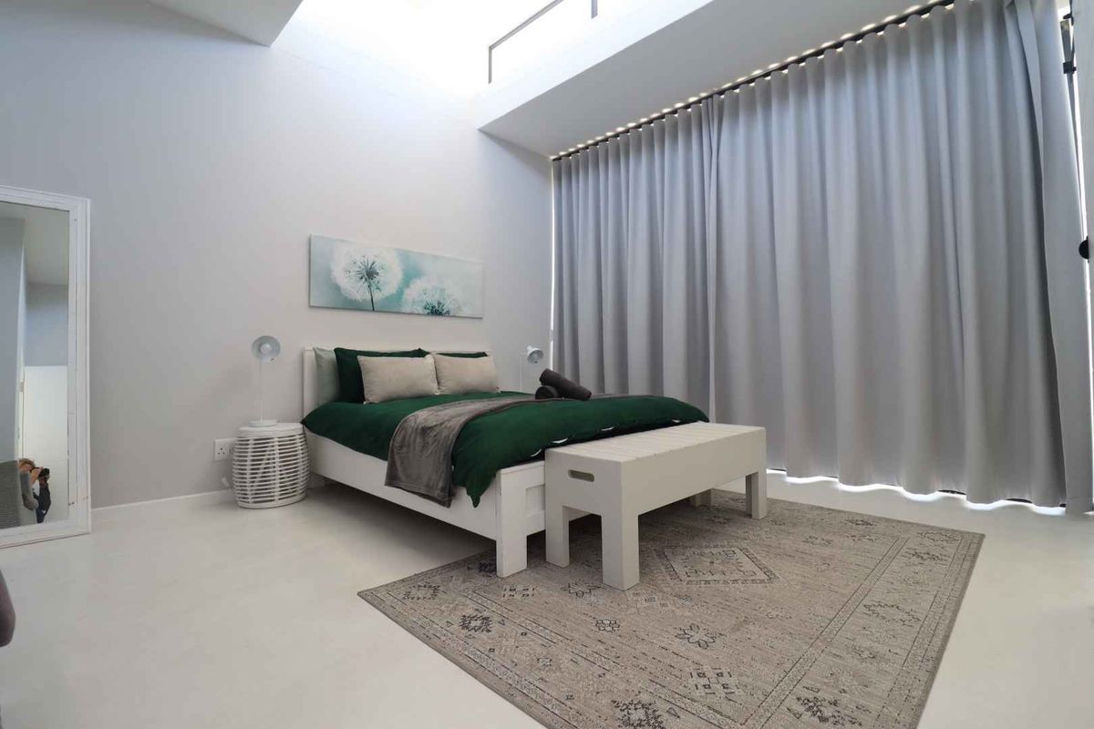 A bright and modern bedroom featuring high ceilings with a skylight, large floor-to-ceiling curtains, and smooth flooring.