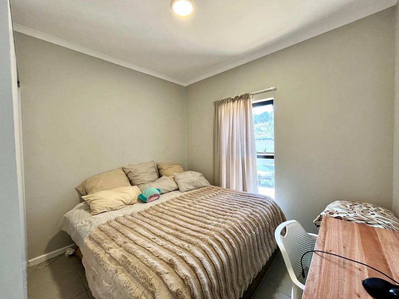 A functional bedroom featuring neutral wall tones, tiled flooring, and a built-in wardrobe, offering a comfortable and practical living space.