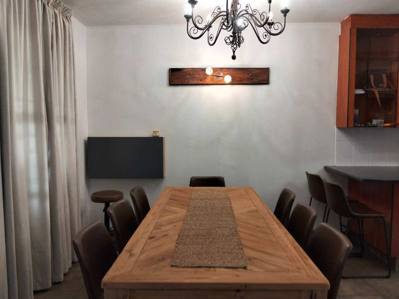 A dining area featuring a central chandelier, wall-mounted lighting, and adjacent kitchen cabinetry with a breakfast counter.