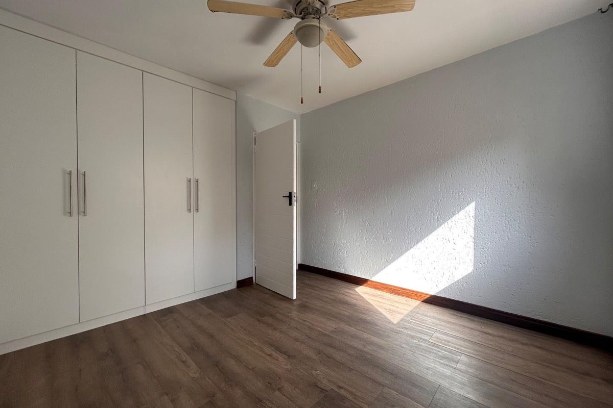 A bright, empty bedroom featuring built-in white cabinetry, wood-look flooring, and a ceiling fan.
