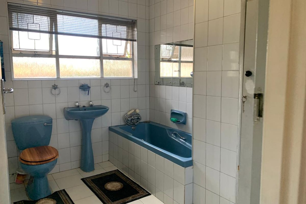 A dated bathroom featuring blue sanitaryware, including a pedestal basin and built-in bathtub, complemented by white wall tiles and tiled flooring.