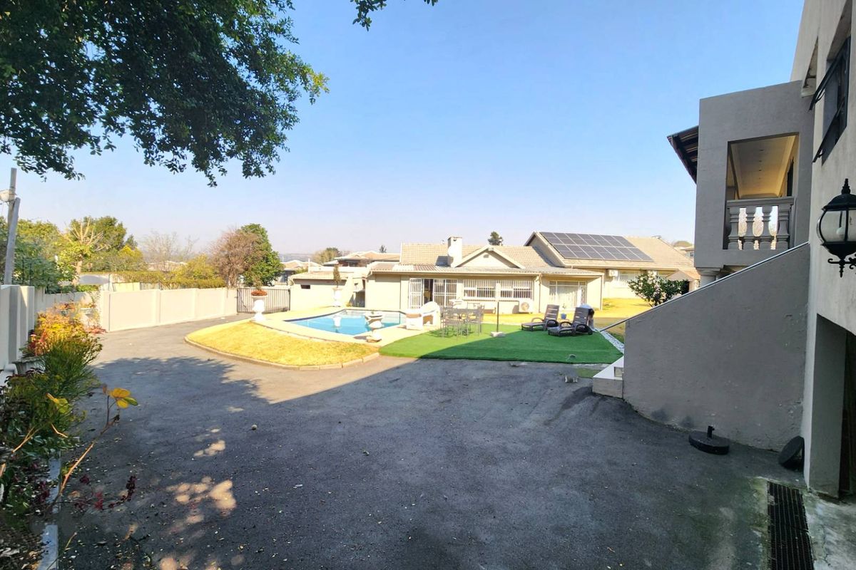 Rear exterior view featuring a swimming pool, artificial lawn area, paved driveway, and solar panels installed on the main roof.