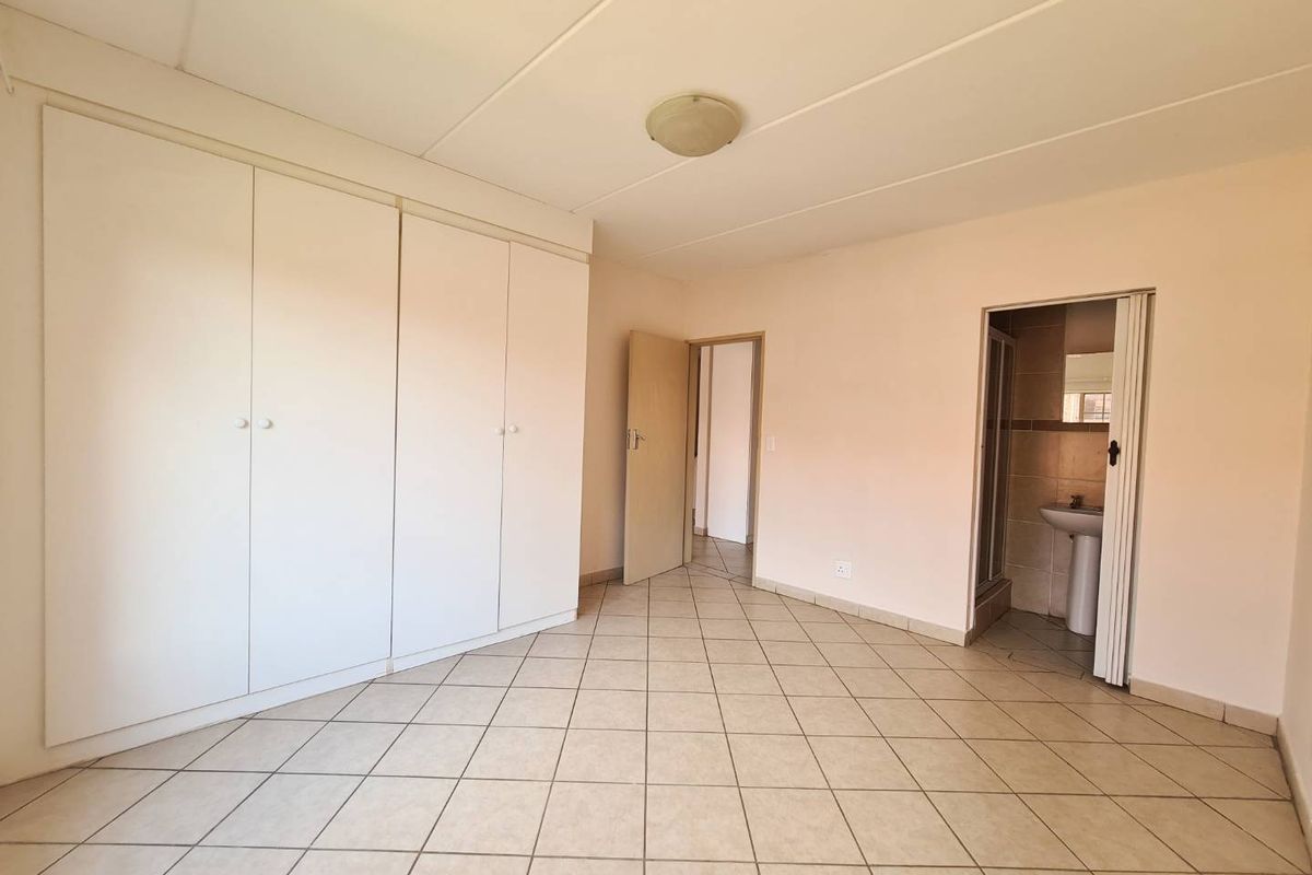 A spacious, empty bedroom featuring neutral tiled flooring, built-in cupboards, and an attached en-suite bathroom.