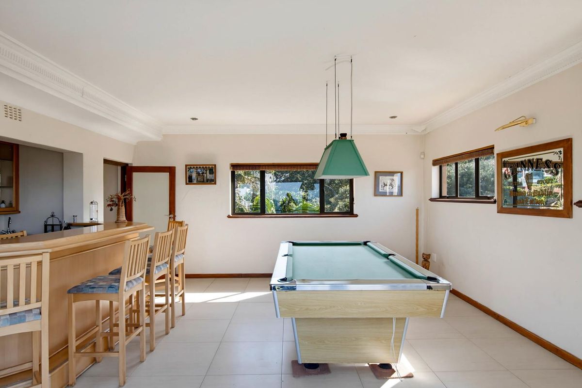A spacious entertainment room featuring a built-in bar, tiled flooring, and large windows providing natural light and garden views.