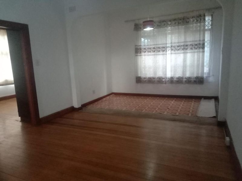 An empty living room featuring polished timber flooring, a raised tiled platform area, and a classic architectural archway.