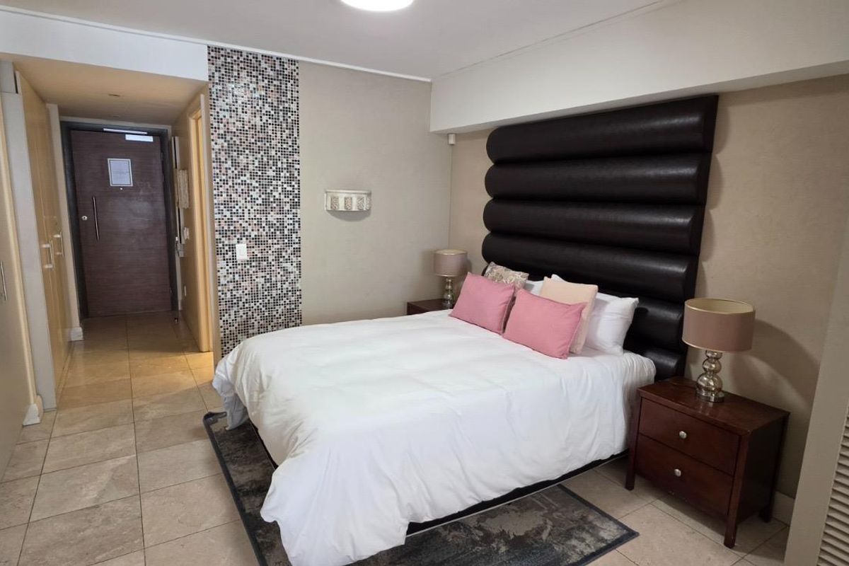 A well-maintained bedroom featuring tiled flooring, built-in cupboards, and a decorative mosaic feature wall.