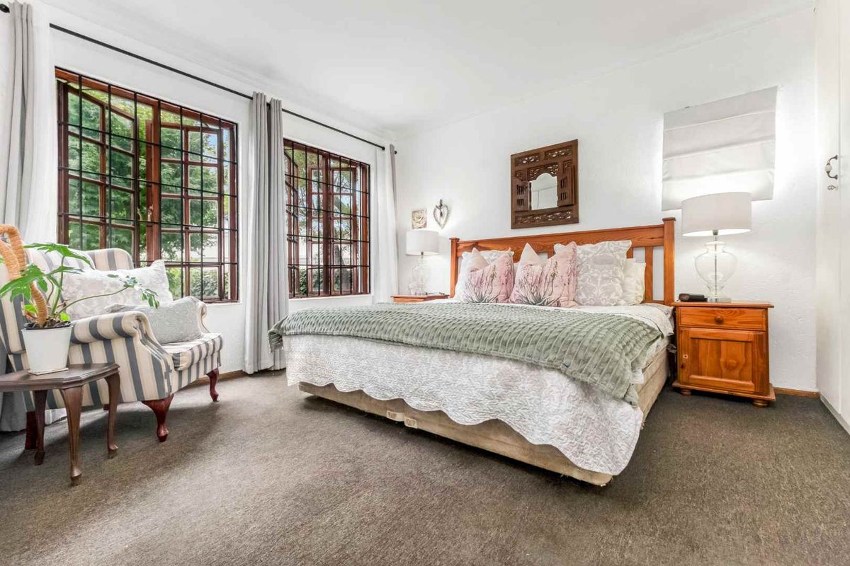 A well-lit bedroom featuring timber-framed windows with security bars, neutral carpeted flooring, and built-in storage.