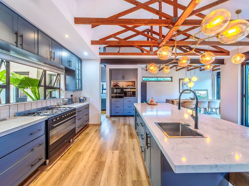 Modern open-plan kitchen featuring a large island with stone countertops, gas hob, exposed timber roof trusses, and high-quality cabinetry throughout.