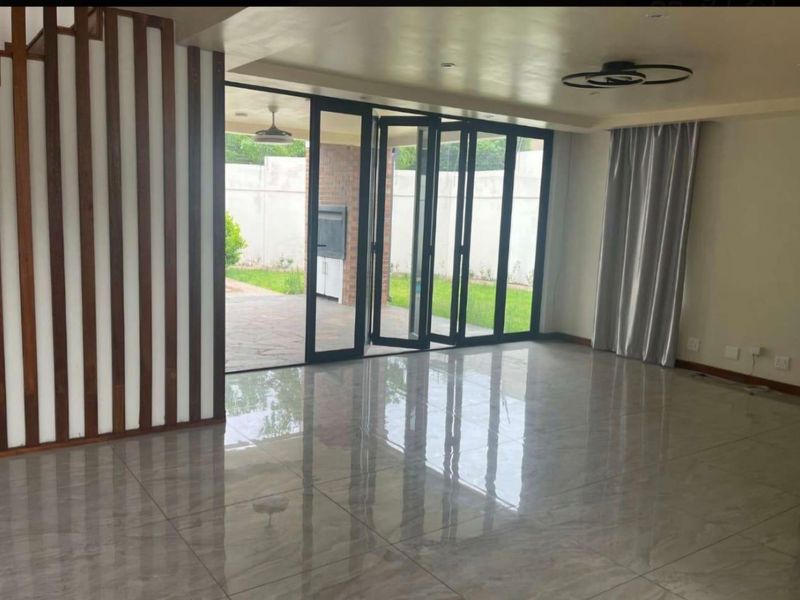 Spacious, modern living area featuring polished porcelain tiles, a decorative wooden slat partition, and large bi-fold doors opening to an outdoor patio.