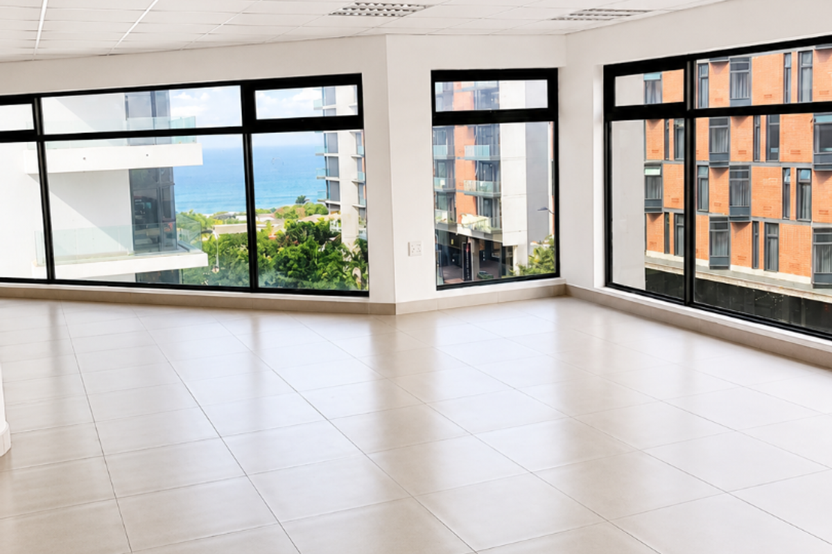 A bright, vacant open-plan office space featuring large windows with scenic views, neutral floor tiles, and a modern suspended ceiling with integrated lighting.