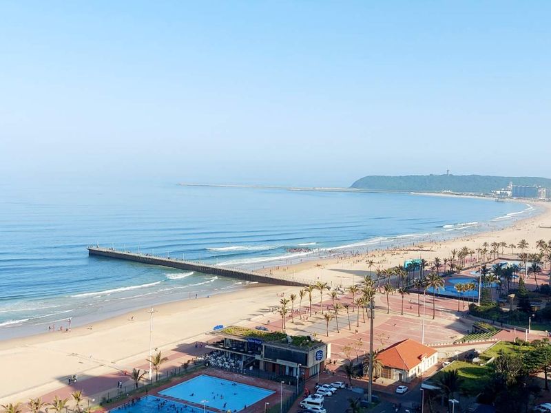 A panoramic elevated view overlooking the coastline, beach, pier, and surrounding urban promenade area.