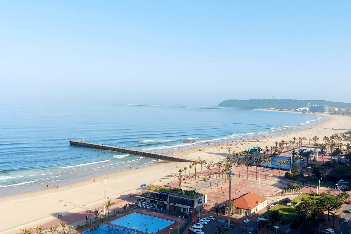 A panoramic elevated view overlooking the coastline, beach, pier, and surrounding urban promenade area.
