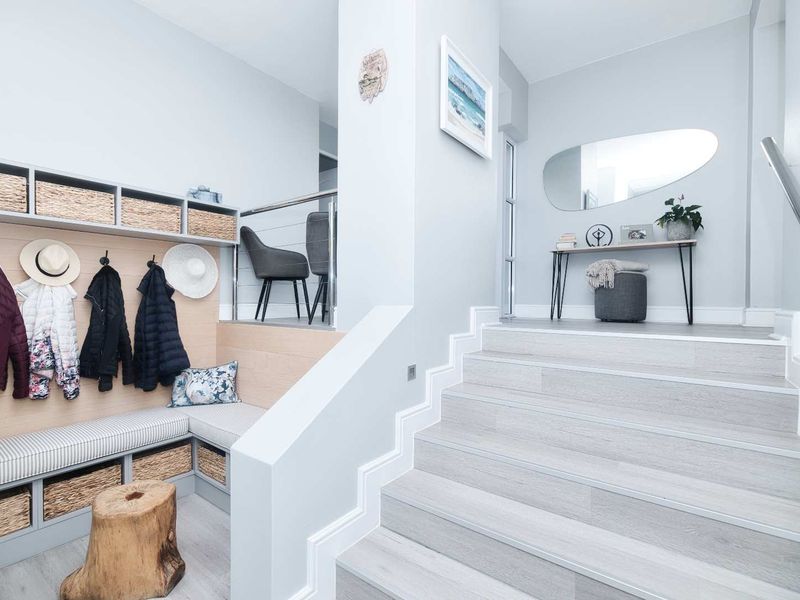 A bright and modern entrance hall featuring a built-in storage bench, light wood-look flooring, and a staircase with a sleek metal handrail.