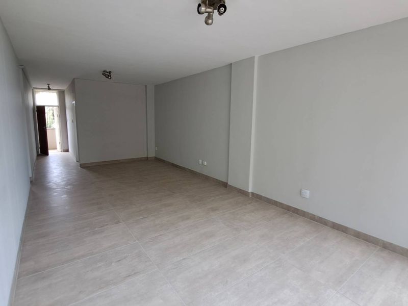 A spacious, empty open-plan living area featuring neutral tiled flooring and clean, freshly painted walls, offering a versatile blank canvas for interior design.