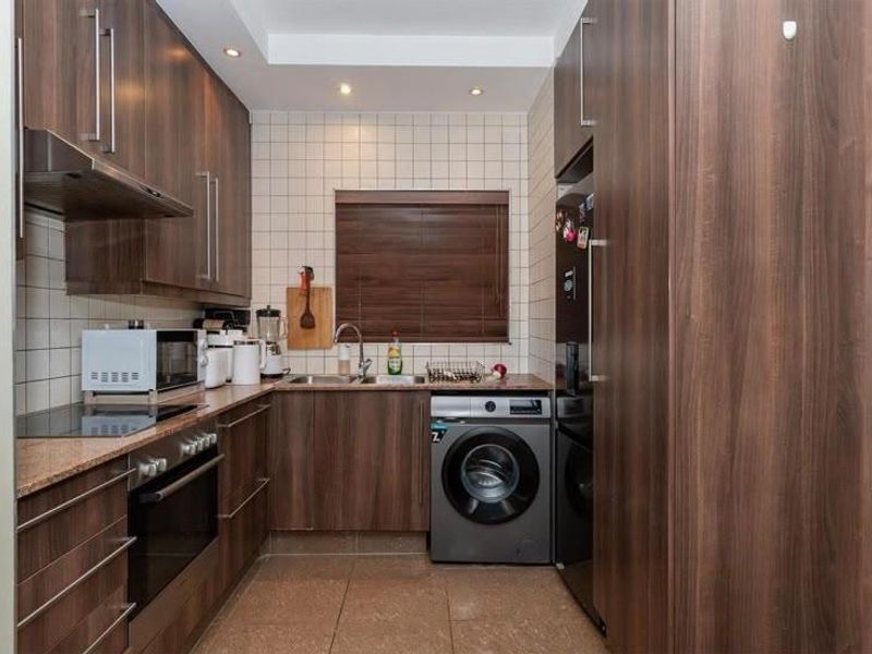 Compact kitchen featuring dark wood-grain cabinetry, integrated appliances, tiled backsplash, and durable tiled flooring, offering a functional and modern workspace.