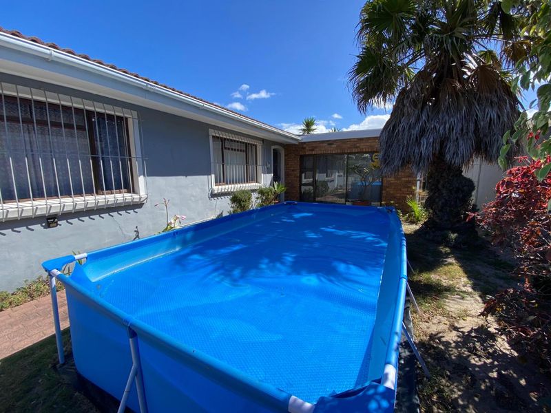Rear exterior view featuring a portable above-ground pool, brick and rendered wall finishes, and security bars on windows.