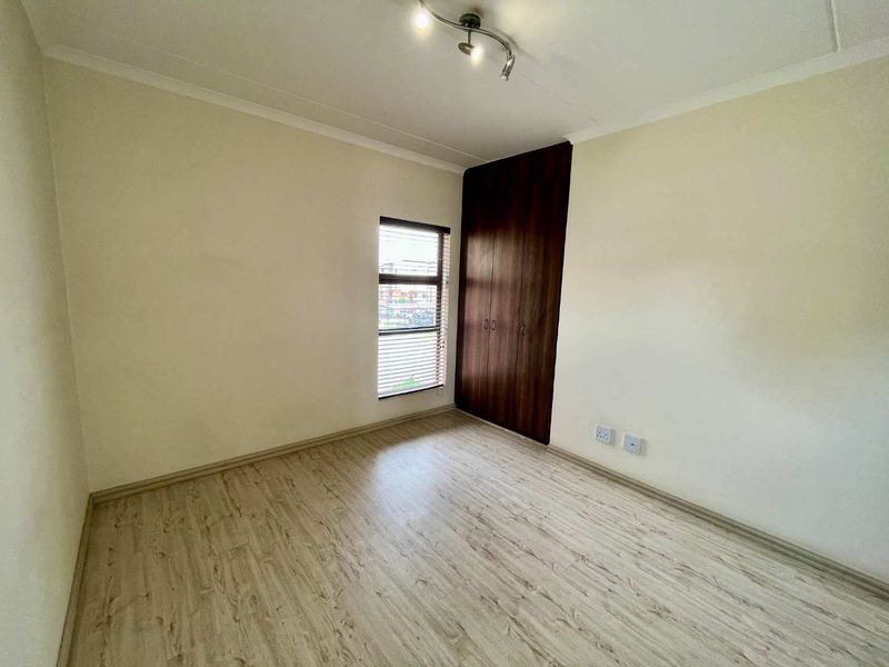 A clean, empty bedroom featuring light-toned laminate flooring, neutral walls, and dark wood built-in cupboards.