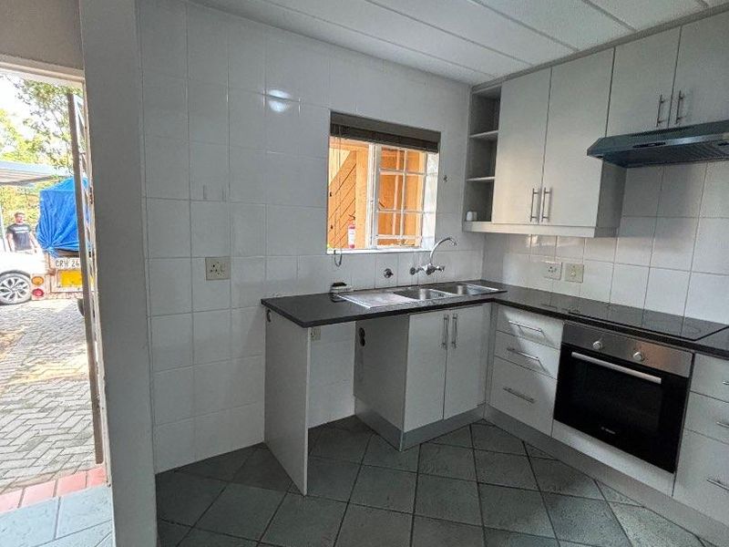 A functional kitchen featuring built-in cabinetry, a stainless steel sink, an integrated oven, and an extractor fan, with direct access to the exterior.