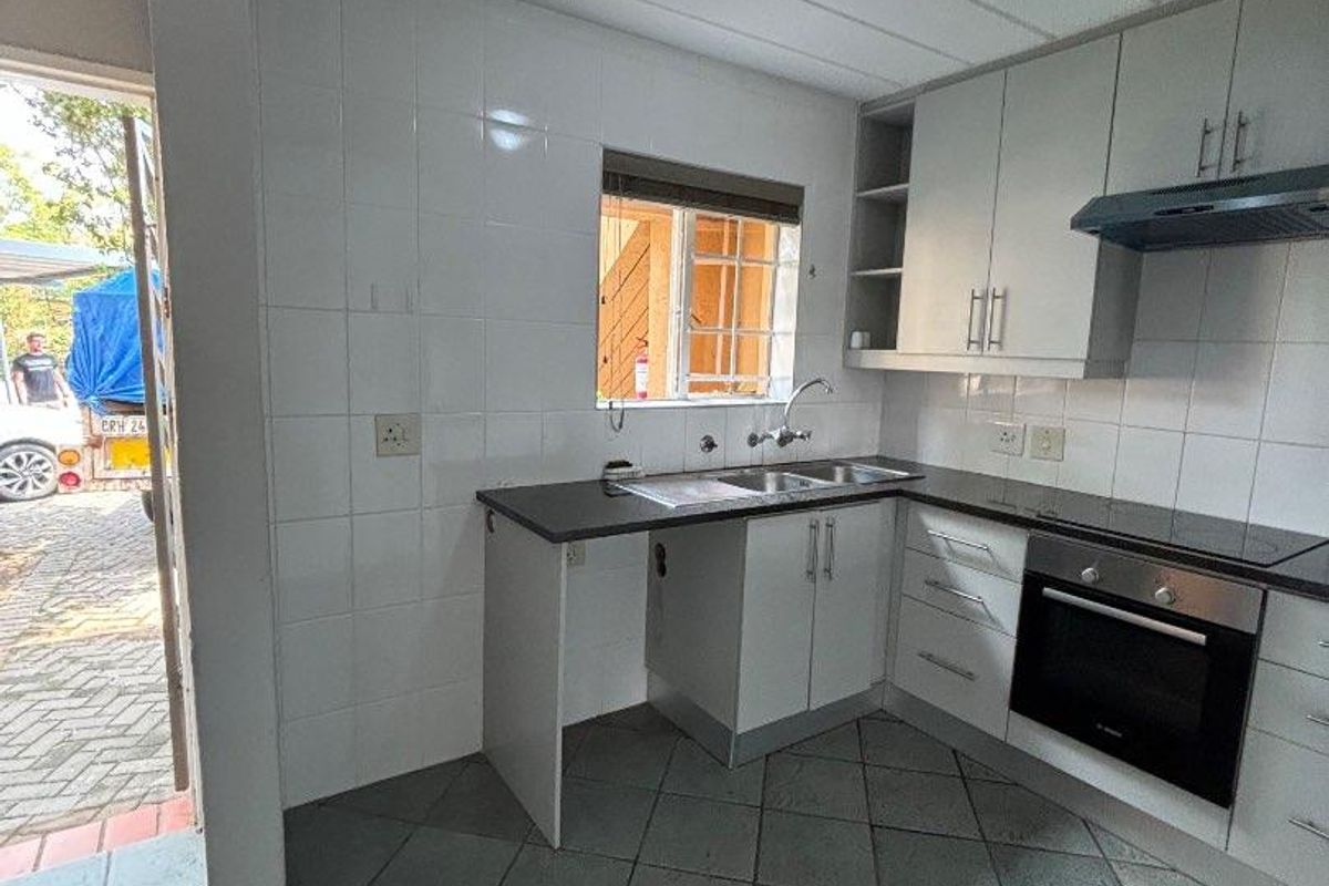 A functional kitchen featuring built-in cabinetry, a stainless steel sink, an integrated oven, and an extractor fan, with direct access to the exterior.