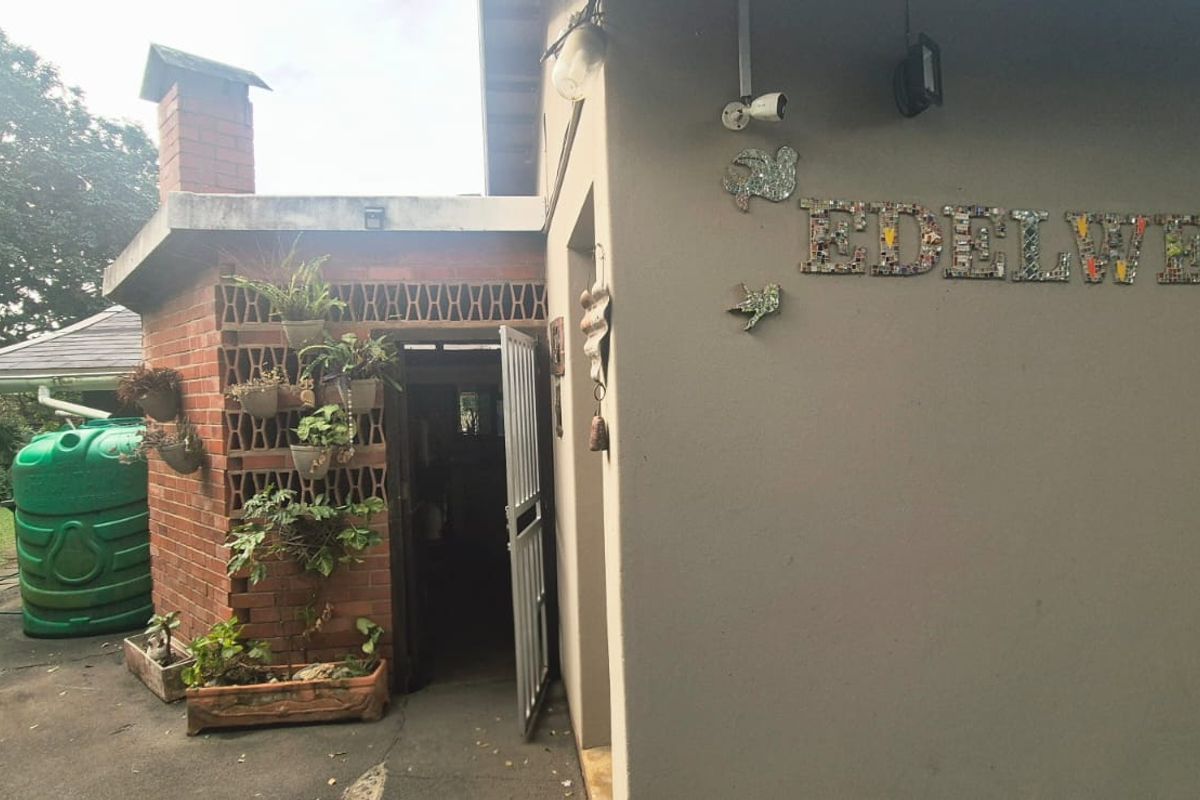 Rear exterior view featuring a brick chimney, breeze block wall, security gate, and a water tank in a garden setting.