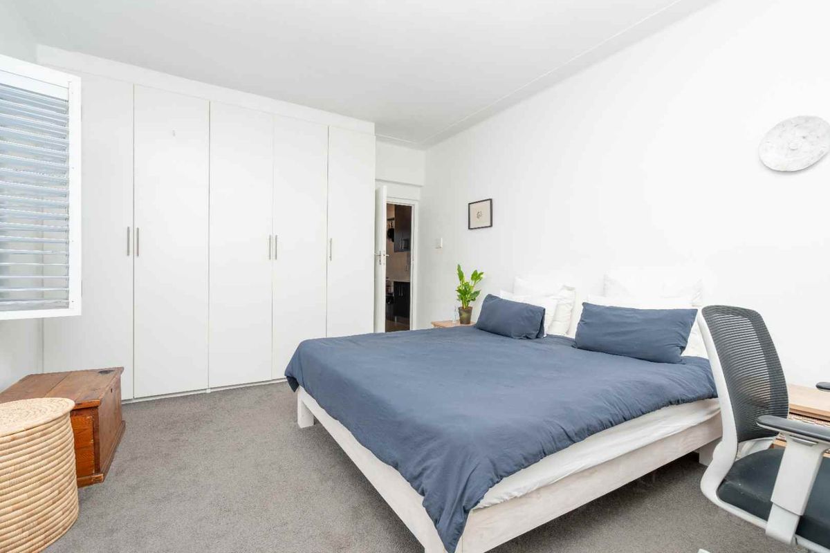 A bright bedroom featuring built-in floor-to-ceiling wardrobes, neutral carpeting, and a window with fitted shutters.