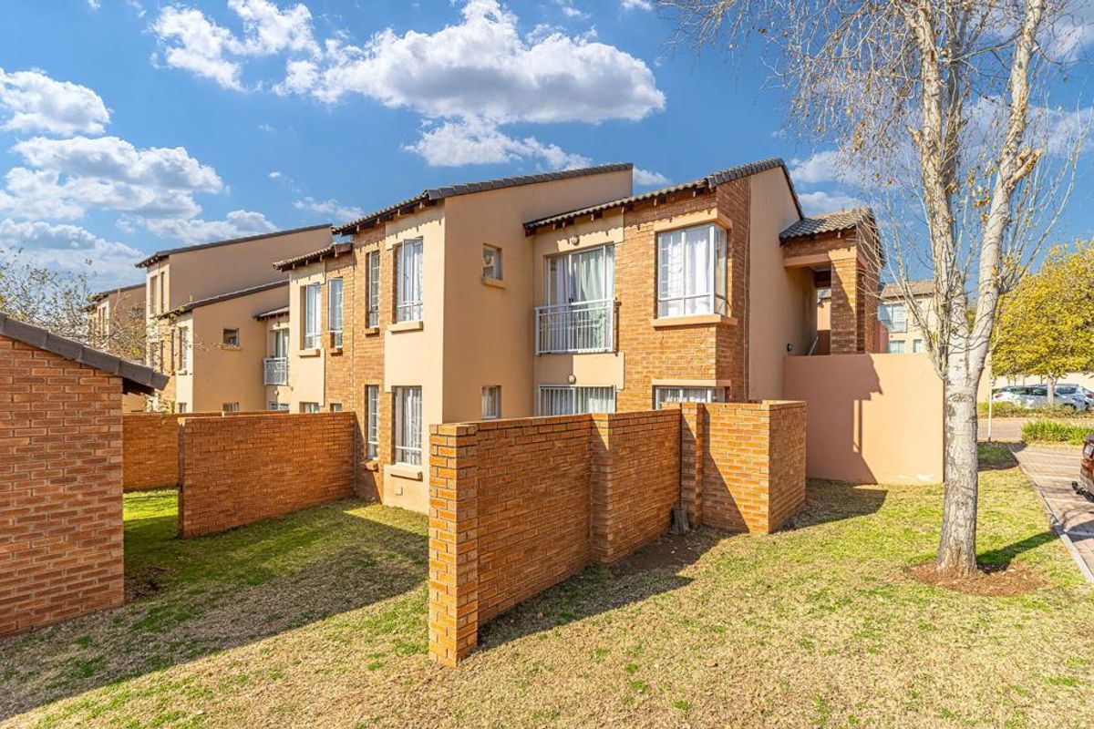Rear view of a multi-story apartment complex featuring face brick boundary walls, private garden space, and upper-level balconies with metal railings.