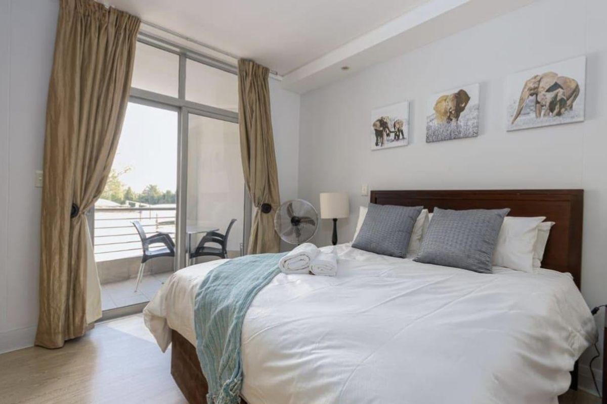 A well-lit bedroom featuring laminate flooring and a large sliding glass door providing direct access to a private balcony.