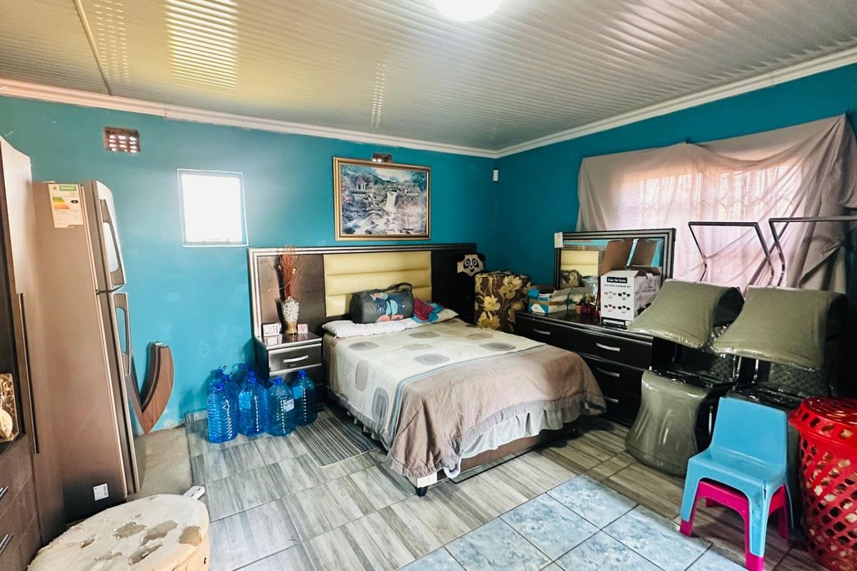 A bedroom featuring tiled flooring and ceiling panels, currently utilized with various personal items and furniture.